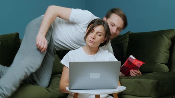 Young Woman That Is Working at the Computer Receiving a Gift From Her Husband alt