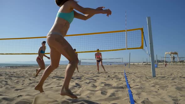 Women teams play beach volleyball at sunset and a player passes the ball. alt