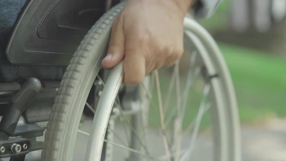 Close-up of Old Male Caucasian Hand Rolling Wheelchair. Unrecognizable Handicapped Man Riding alt