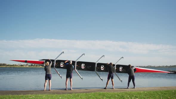 Four senior caucasian men and women carrying a rowing boat together alt