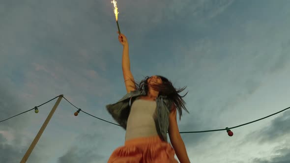 Low angle view of happy woman jumping with firework candle alt