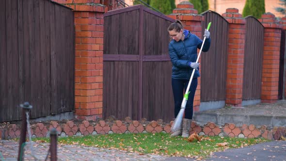 girl removes fallen leaves with a rake from the lawn in front of the house alt