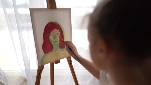 Beautiful Young Artist Paints a Portrait with Oil Paints Sitting at Home in Front of the Window alt