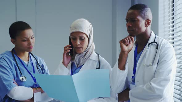 Front view of Middle-East female doctor talking on mobile phone with her colleagues in hospital alt