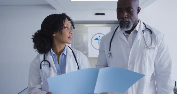 African american male and female senior doctors discussing over medical reports at hospital alt