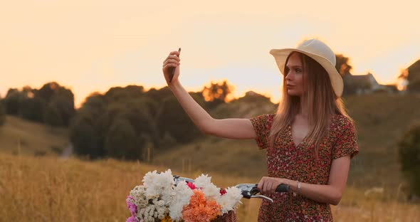 Girl with a Bike in a Hat Makes a Selfie Using a Smartphone alt