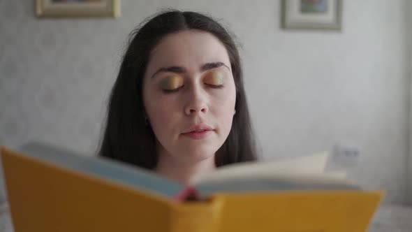 A Young Woman Reads a Book and Rubs Her Eyes with Fatigue and Irritation alt