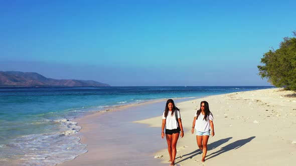 Modern smiling girls travelling by the sea on beach on clean white sand and blue background 4K alt