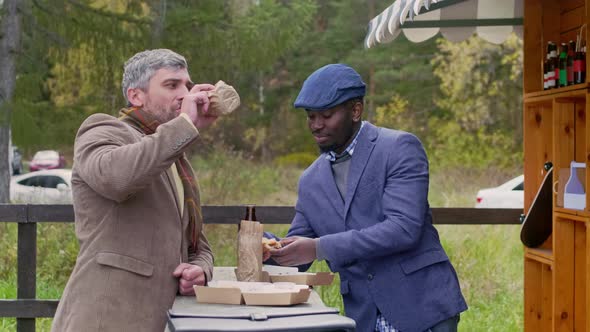 Two speaking men eating burgers by food trailer