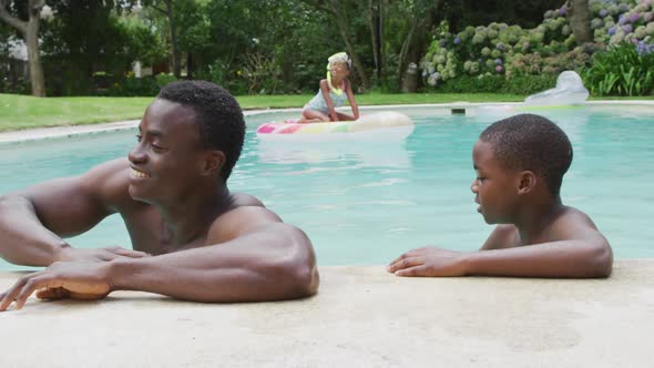 Happy african american father and son relaxing in pool alt