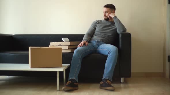 Tired Delivery Man in Casual Clothes Waiting for Client While Sitting on Sofa in Spacious Lobby alt
