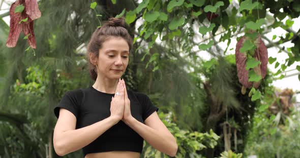 Portrait of a Brunette Woman Doing Yoga in a Botanical Garden and Meditating
