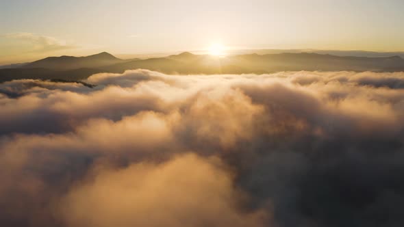 Aerial drone view of Sunrise over clouds. Flying above morning Fog in the Mountains.  alt