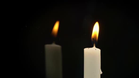 White Paraffin Candle with Yellow Tints Burns on Black Background in Reflection alt