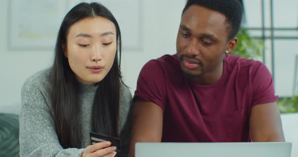 Cheerful Young Mixed Ethnicity Couple Shopping Online While Sitting Home with Credit Card and Laptop alt