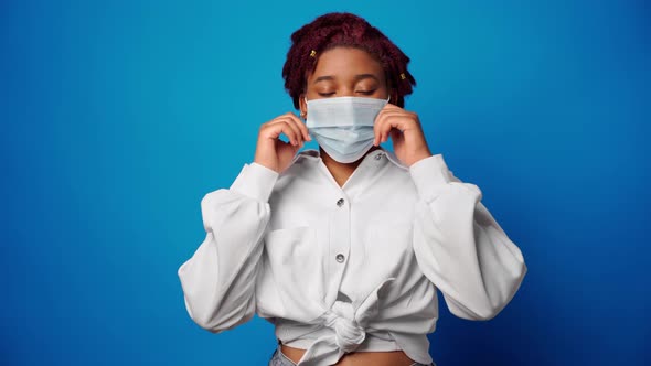 Young Afro Woman Takes Off Medical Mask and Smiles Against Blue Background