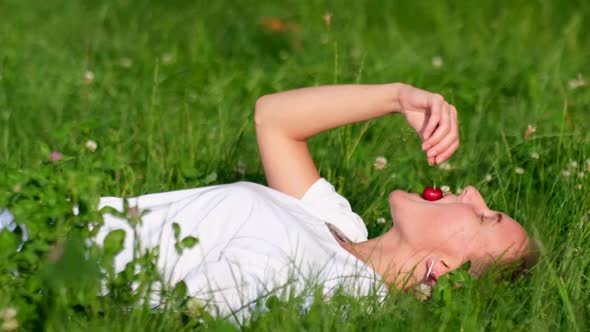 Beautiful Young Woman Lying on the Grass Enjoying Cherries alt