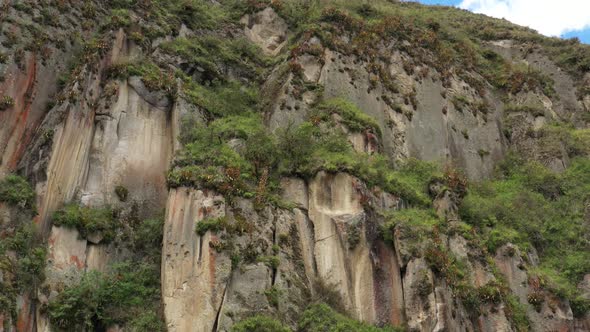Approaching a cliff with grey brown and red colors that is covered in grass and bromelias alt