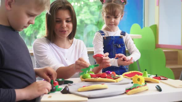 Caucasian girl and boy kid playing and learning at preschool with female teacher. Mother, daughter a