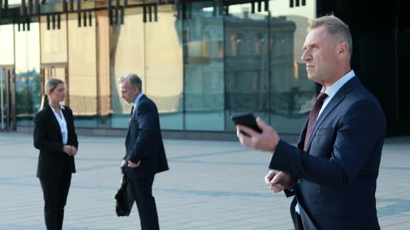 A Man in a Business Suit Is Arguing on the Phone Against the Backdrop of a Multi-storey Modern