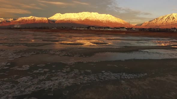 Flying over lake shoreline towards houses during colorful sunset alt