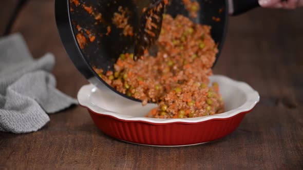 A minced meat and vegetable mixture being placed to a baking pan. Making shepherd's pie.