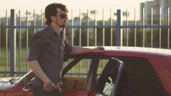 Portrait of Handsome Man with His Old Classic Powerful Car on Street at Sunset or Sunrise alt