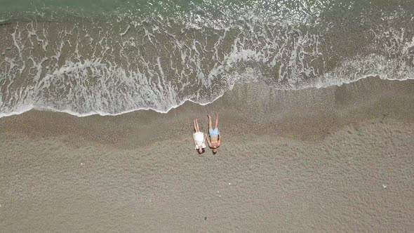 Couple Resting on Sand Near Waving Sea