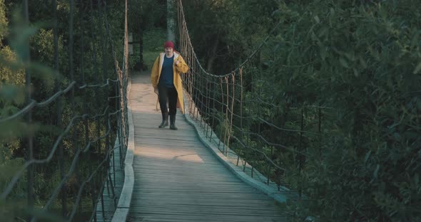 Man Hiking Tourist in Yellow Raincoat Walking Along Wooden Suspension Bridge