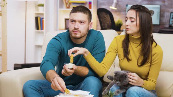 Concentrated Young Couple Sitting on Couch Eating Fried Chicken alt