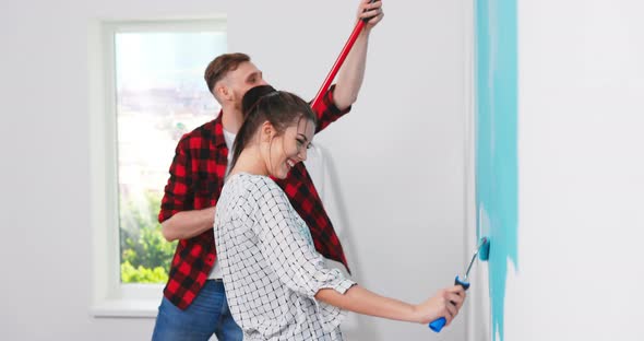 Cute and Beautiful Young Caucasian Woman Painting Walls in the Apartment in Blue Color with alt