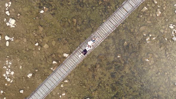 Aerial Top Down View of Young Couple in Love Lying Together on Wooden Bridge Over River