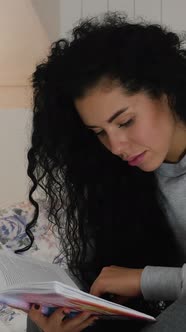 Vertical Video of Young Beautiful Curly Brunette Reading Book in Bed