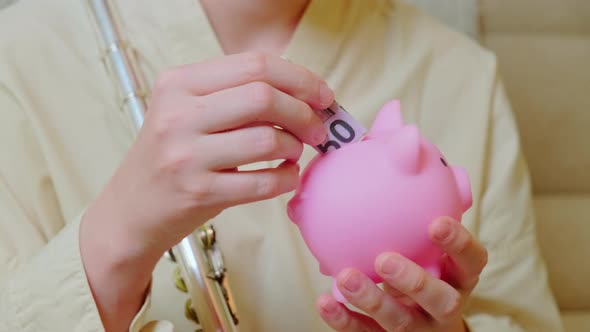 Woman musician with piggy bank at home on sofa in living room