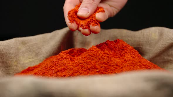 Human hand holds and press a pinch of a red pepper powder by a hand over a sac