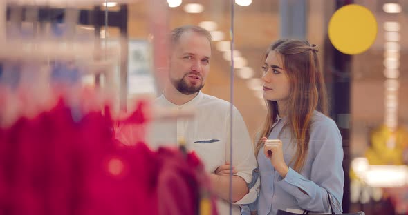Couple is Standing and Discussing Something Next to the Shopping Window in the Mall alt