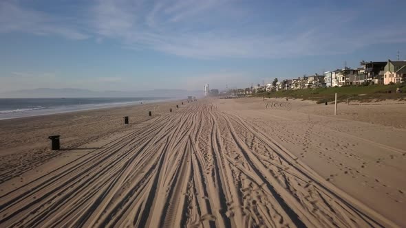 aerial shot at golden hour, going forward above the sand of manhattan beach, with car prints on the alt