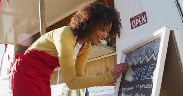African american woman wearing apron writing on food menu slate board of the food truck alt