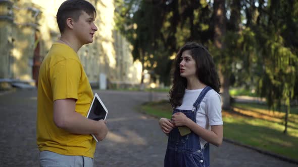 Confident Positive Young Caucasian Woman Talking with Man Standing at College Campus Outdoors alt