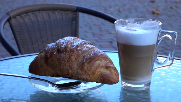 Croissant and fresh prepared latte coffee in a glass, breakfast in a sidewalk cafe.