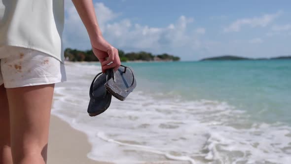 Slow motion of a beautiful young asian woman holding slipper and strolling on the beach