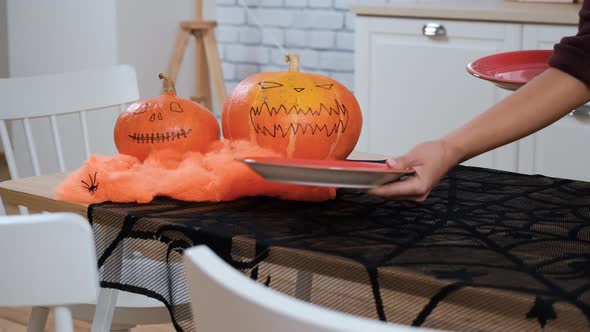 Woman Putting Plates on Festive Halloween Table alt