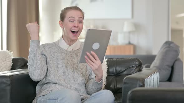Excited Young Woman Celebrating Success on Tablet at Home  alt