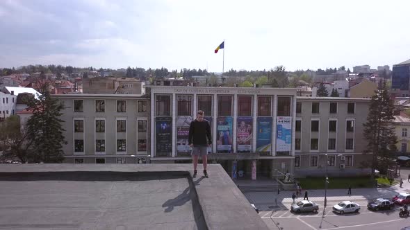 Aerial Drone Shot Pulling Back to Reveal a Young Adult Male Parkour Runner Standing on the Edge of a alt
