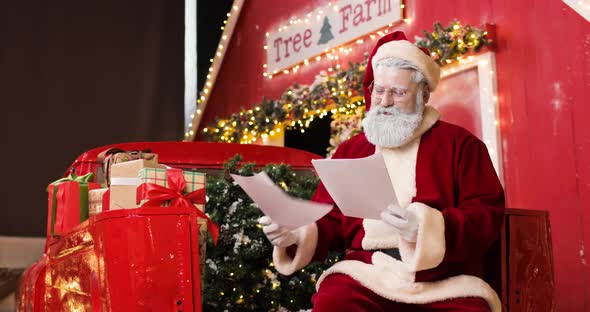 Portrait of a Cute Santa Claus Reading Letters in a Beautiful New Year's Decorated Studio