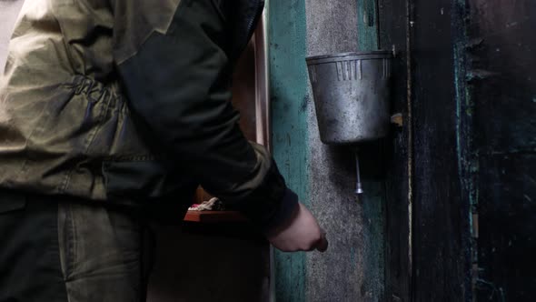 Person in working clothes is washing dirty hands using metal washstand