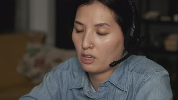 Close-Up of a Young Asian Woman Wearing Headphones with a Microphone for Work alt