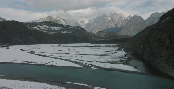 Aerial Dolly Over Hunza River With Tilt Up View Across Epic Snow Capped Mountain Range In Distance. alt