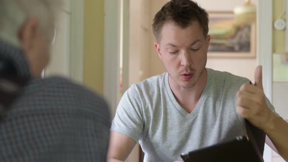 Grandfather And Grandson Talking While Using Digital Tablet By The Window alt