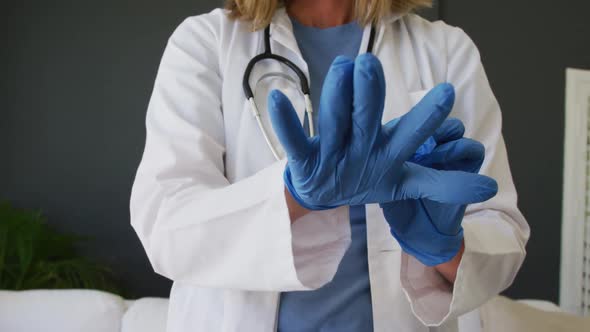 Midsection of caucasian senior female doctor putting on surgical gloves alt